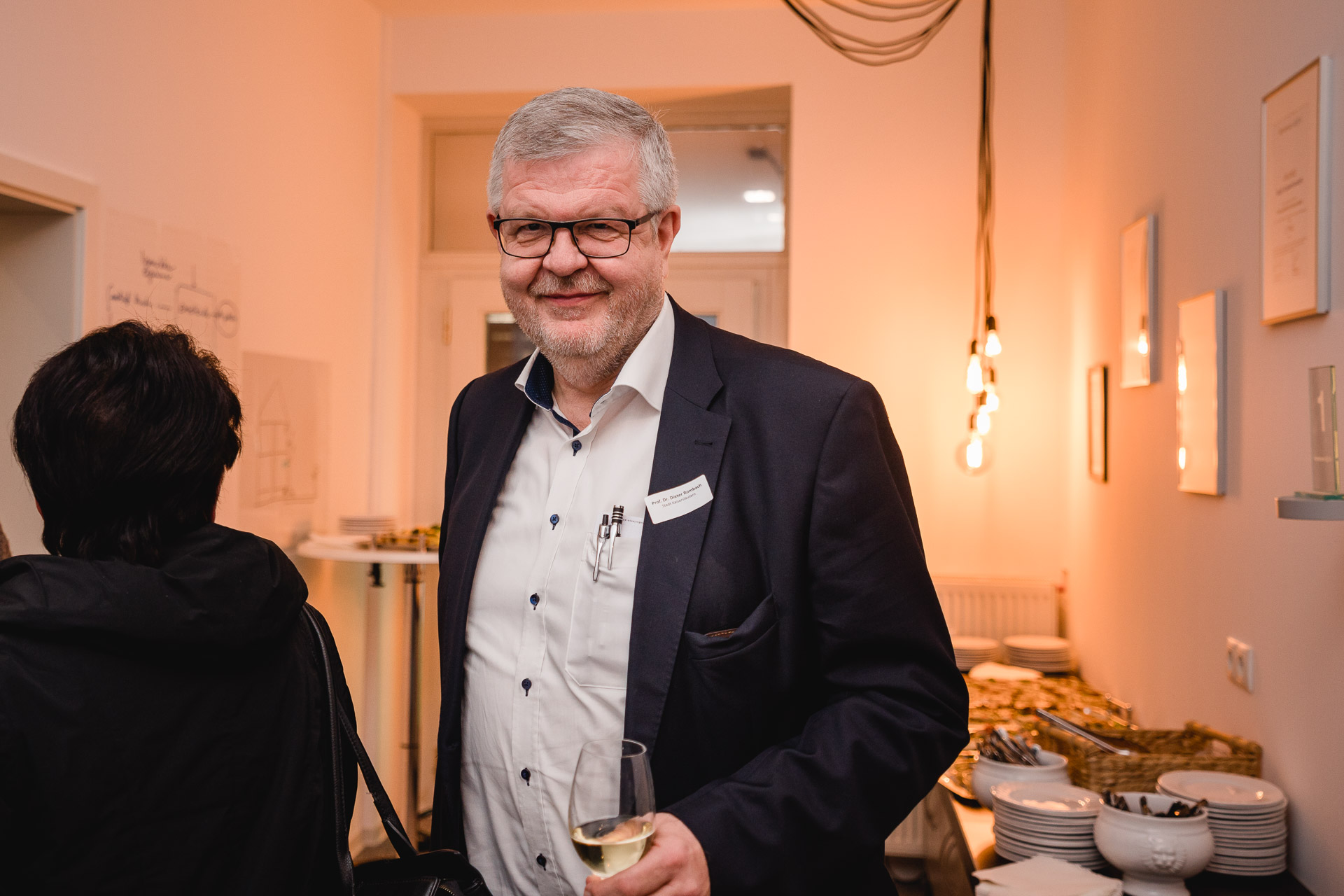 Ein Mann (Prof. Dr. Dieter Rombach) läuft durch einen Zwischenraum, in dem ein Buffet steht.