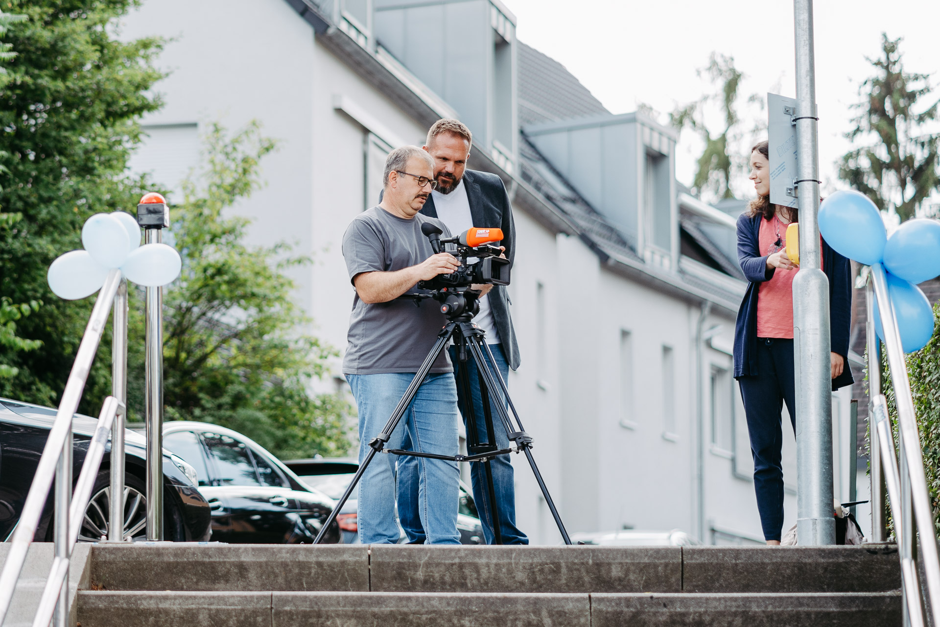 Zwei Männer stehen an einer Kamera und filmen eine Reporterin, die einen Knopf an einer Straßenlaterne im Fauthweg betätigt.