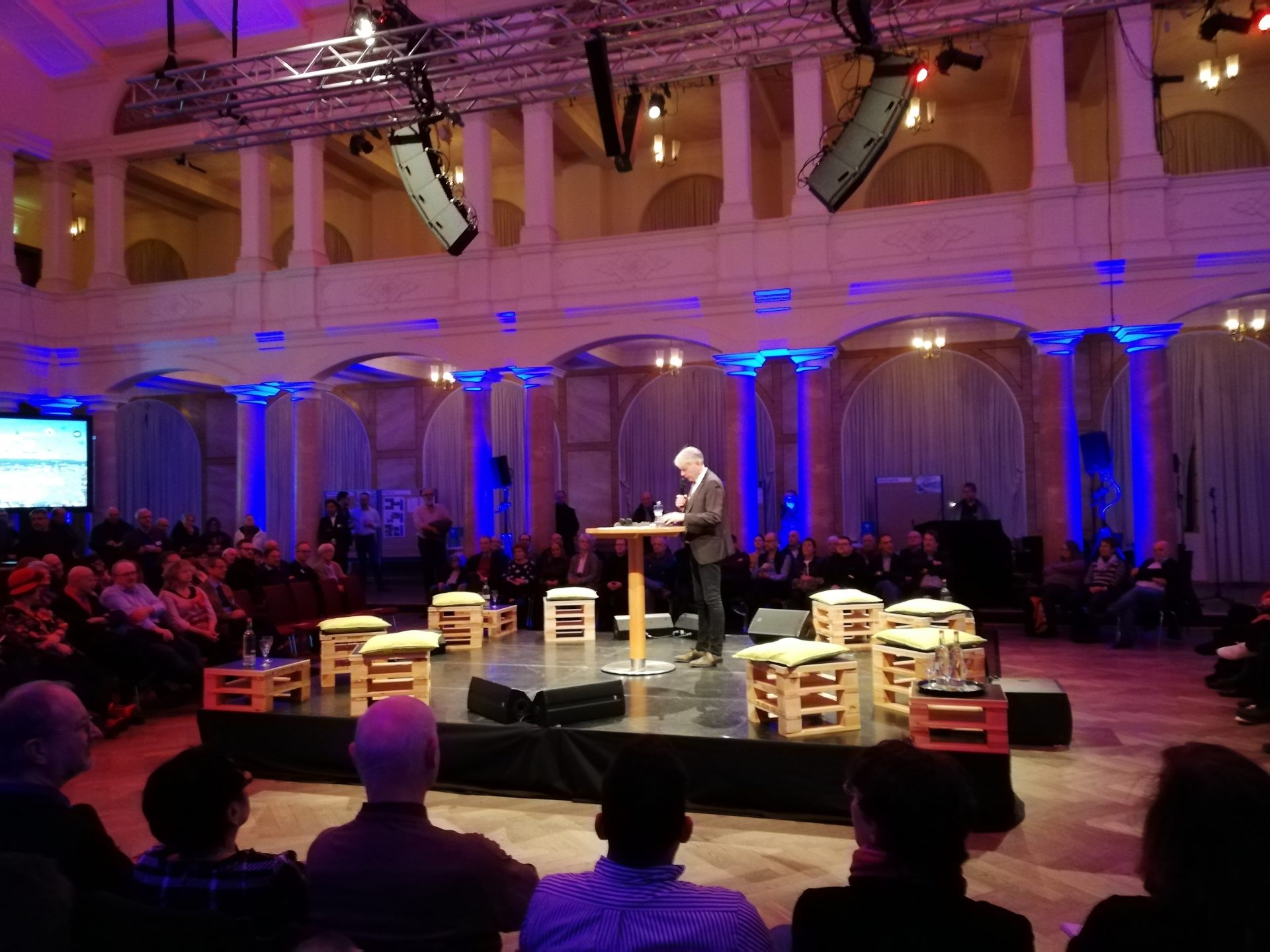 Der Oberbürgermeister steht bei der Eröffnung der Veranstaltung auf einer Bühne inmitten des Publikums.