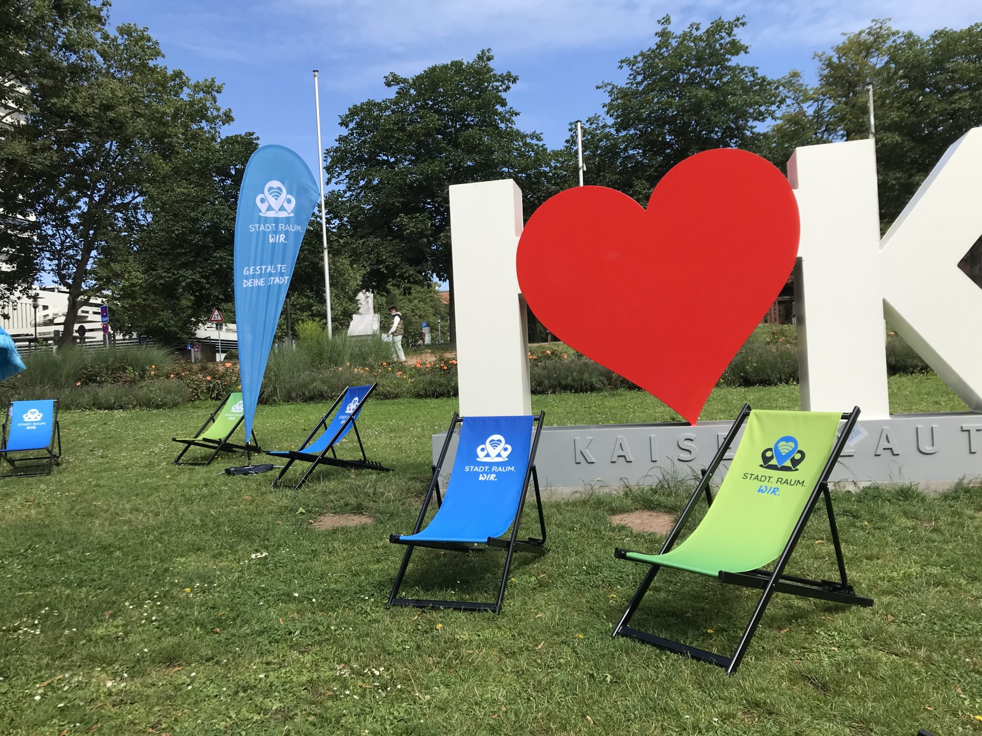 Mehrere Liegestühle stehen auf einer Wiese vor einer Skulptur