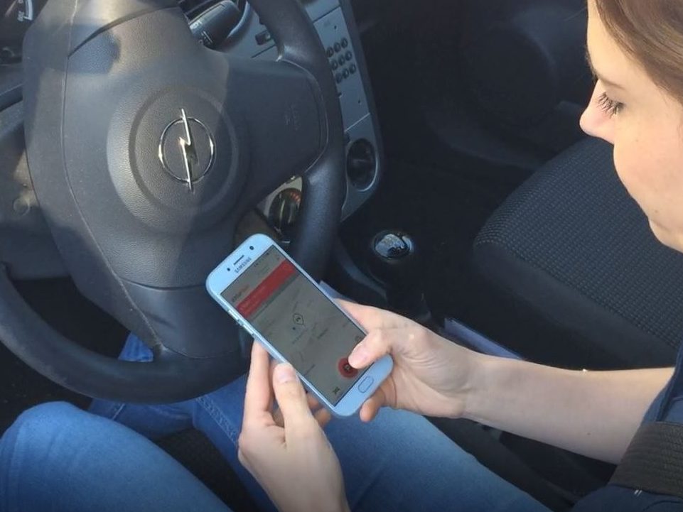 Eine Frau sitzt in einem Auto und schaut auf ihr Handy