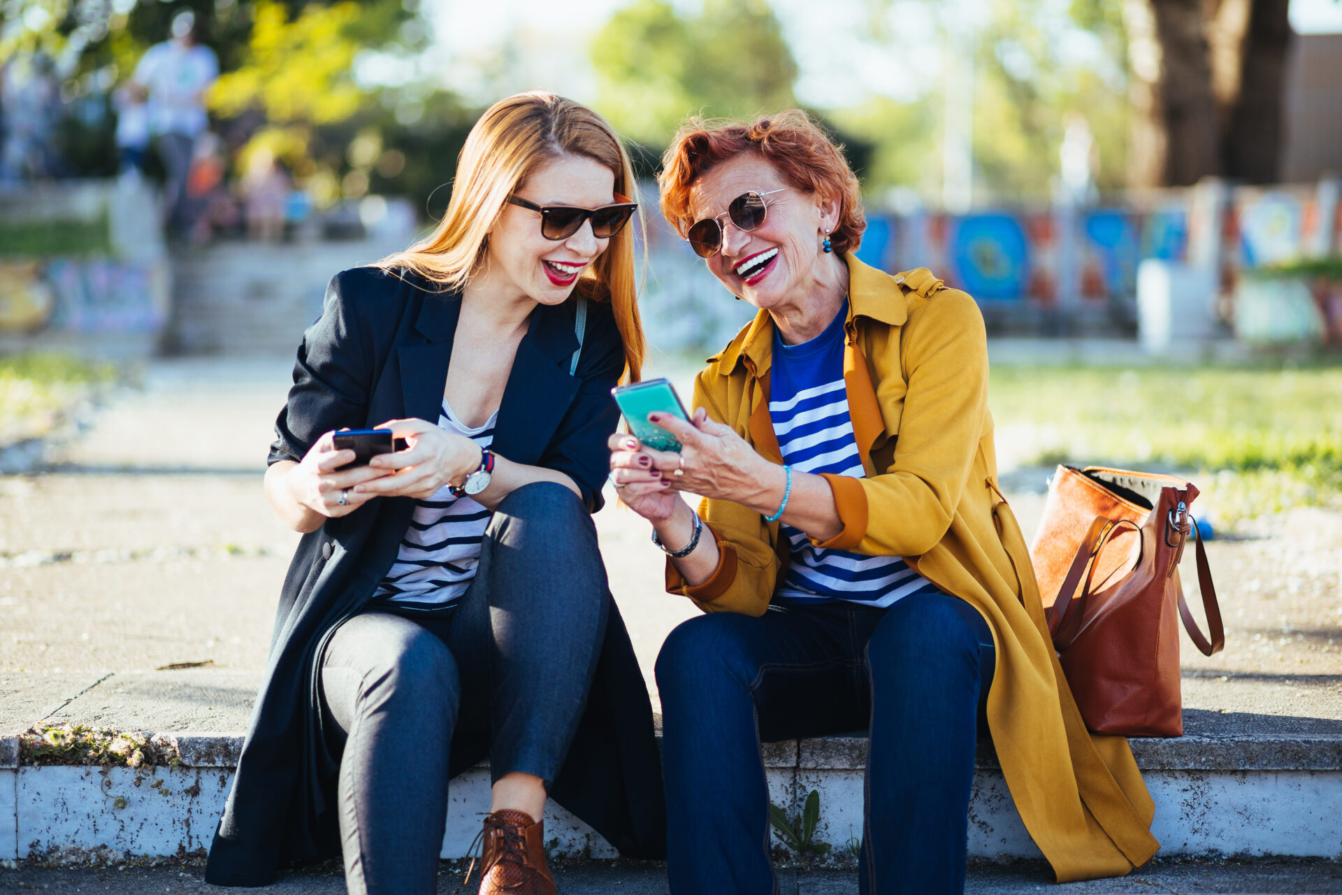 Zwei Frauen sitzen im Freien auf einer Stufe und schauen auf ein Handy