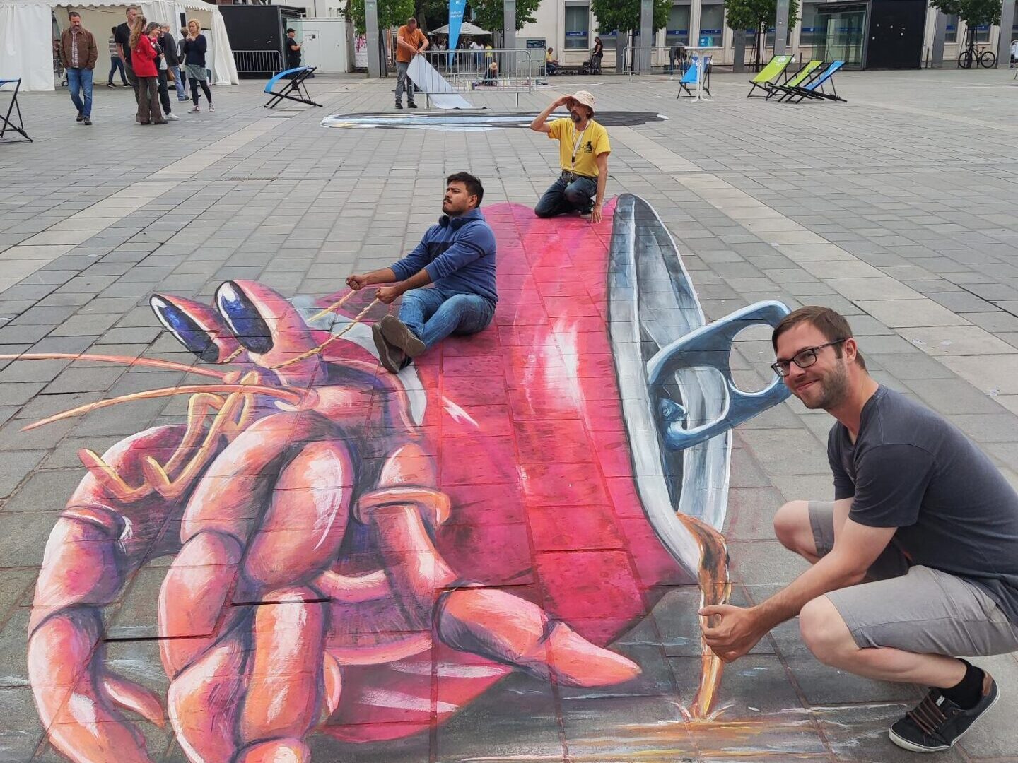 Drei Mämmer posieren auf einem Straßenkunstwerk auf dem Boden, das eine Krabbe zeigt