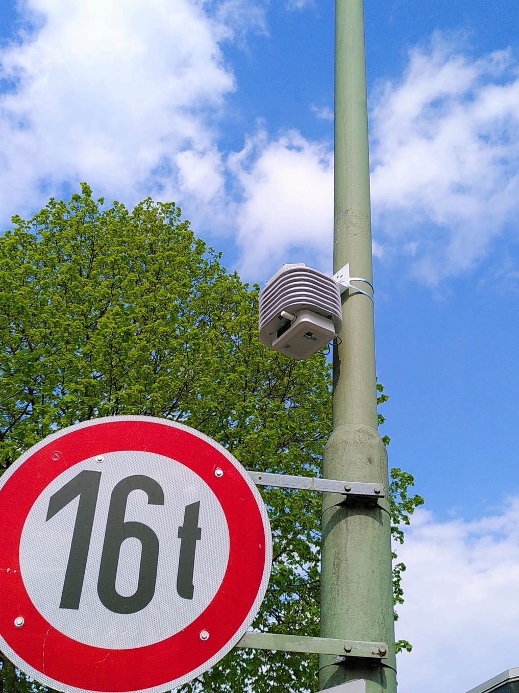 Ein Laternenmast mit einem Straßenschild mit der Aufschrift 16t, darüber ein kleiner grauer Kasten. Im Hintergrund ein blauer Himmel.