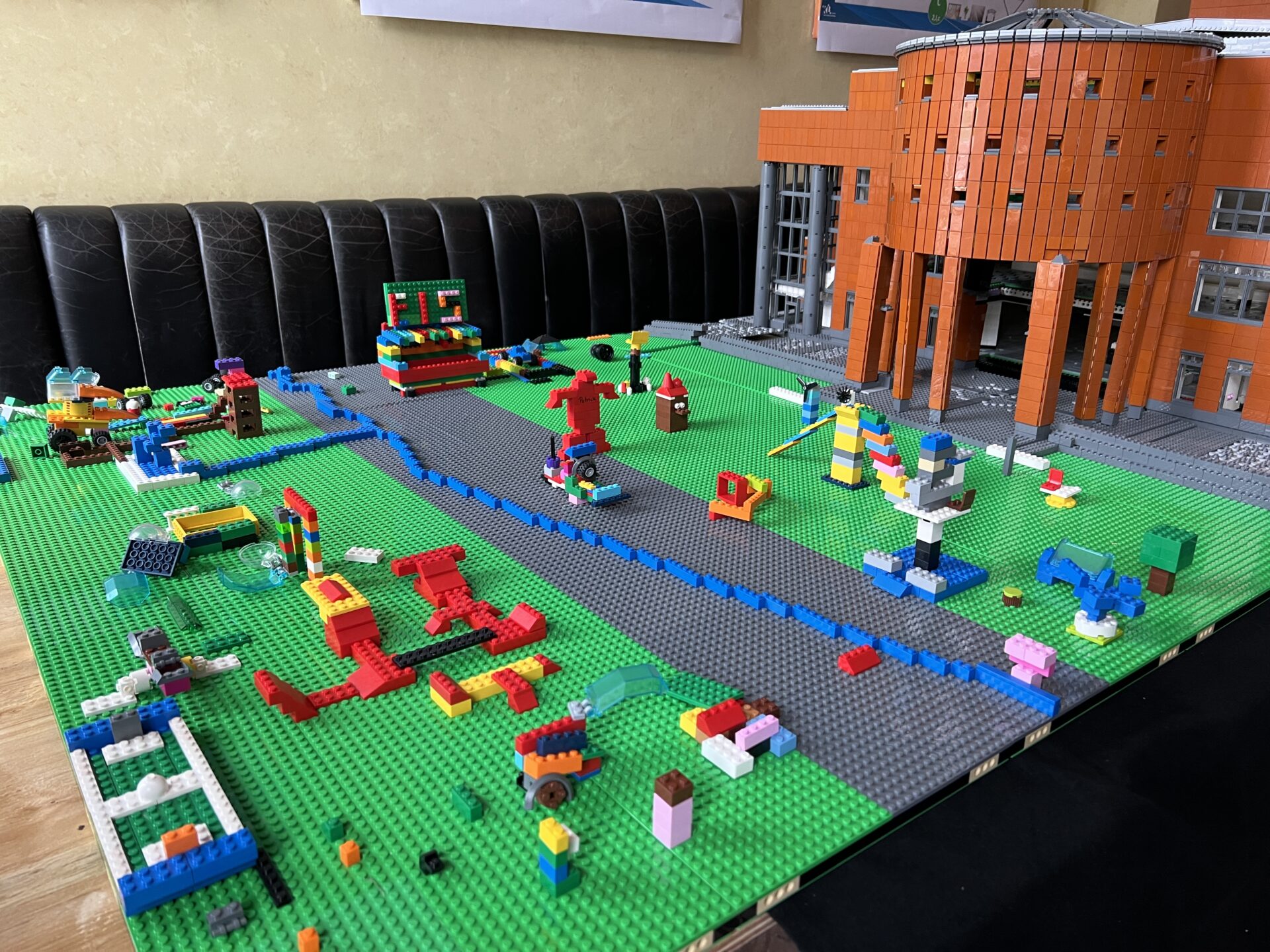 Eine Legobauplatte mit verschiedenen gebauten Legoelementen darauf. Im Hintergrund das Legomodell eines großen Gebäudes (Pfalztheater Kaiserslautern)