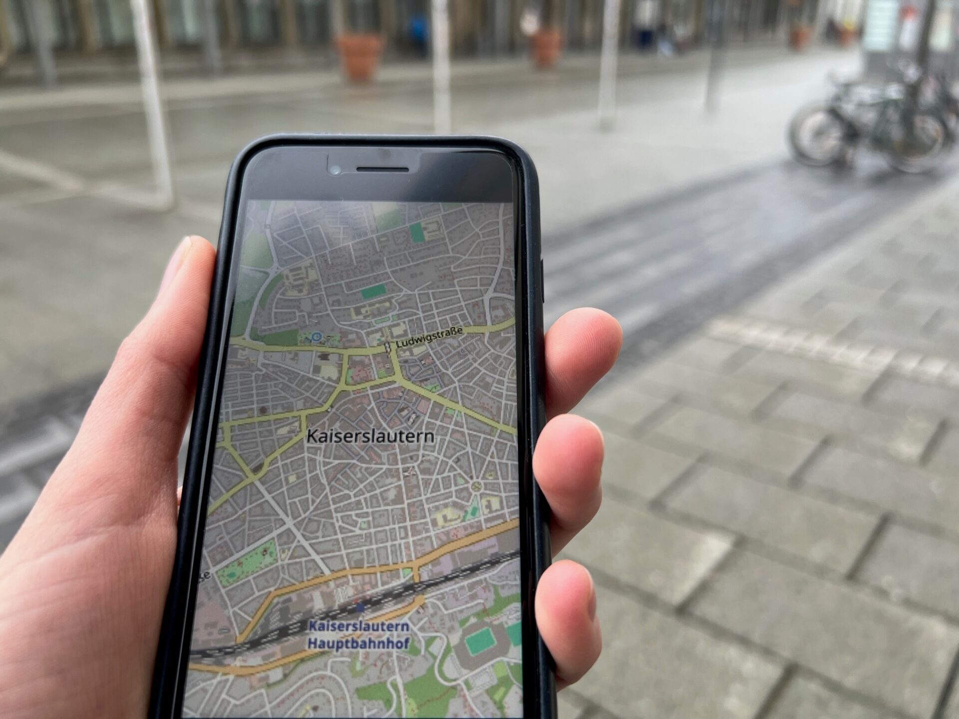 Eine Hand hält ein Smartphone, auf dem eine Straßenkarte von Kaiserslautern zu sehen ist.
